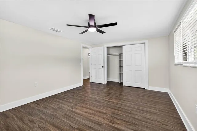 an empty room with wooden floor ceiling fan and windows
