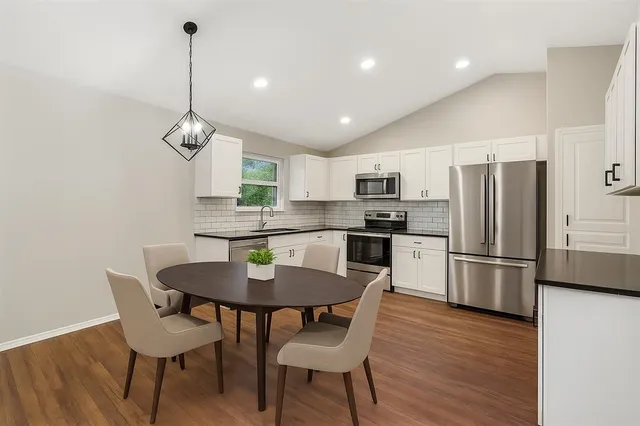a kitchen with stainless steel appliances granite countertop a dining table chairs refrigerator and microwave