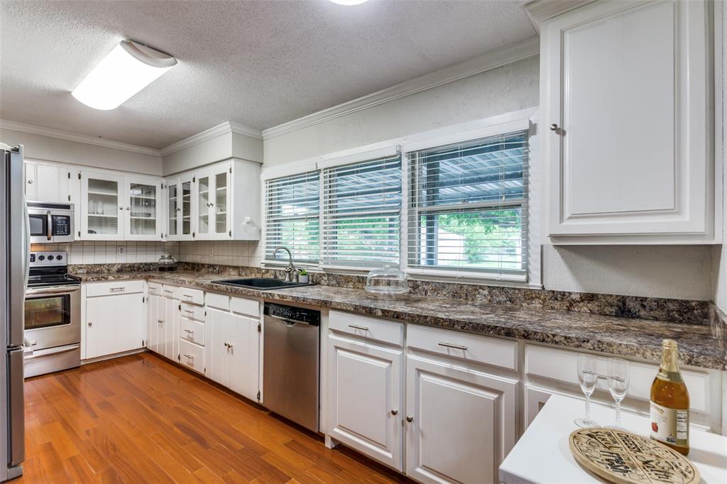 227 North 9th Street Jacksboro, TX 76458 - Photo 6 of 14 a kitchen with stainless steel appliances granite countertop a sink cabinets wooden floor and a window