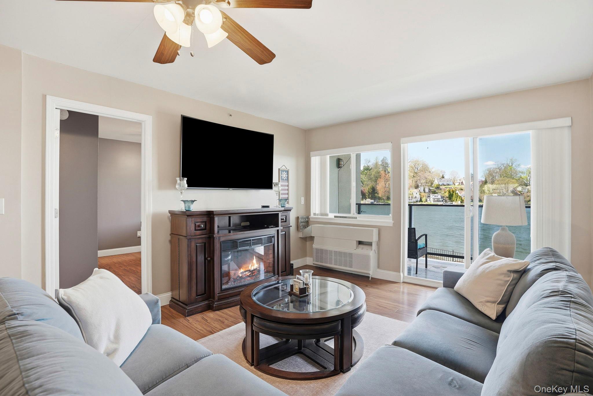 Living area featuring wood flooring, a ceiling fan, a fireplace, and large windows with a water view