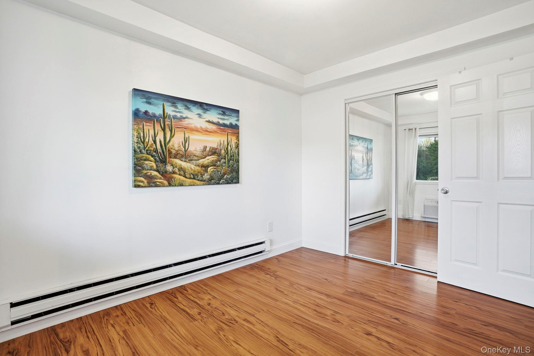 4 Marina Drive, Unit D2 Mahopac, NY 10541 - Photo 21 of 39 Bedroom featuring hardwood floors, a wall-mounted heater, and a closet with mirrored sliding doors