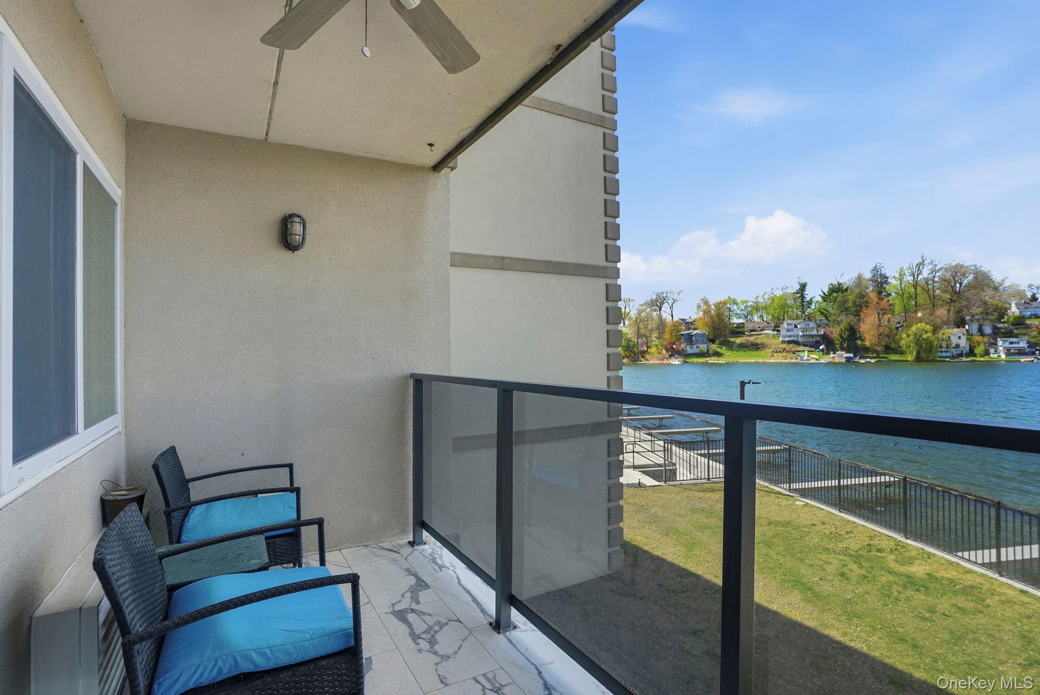 4 Marina Drive, Unit D2 Mahopac, NY 10541 - Photo 24 of 39 This private balcony features a ceiling fan, outdoor lighting, and a glass panel railing, offering views of the expansive body of water and the distant shoreline