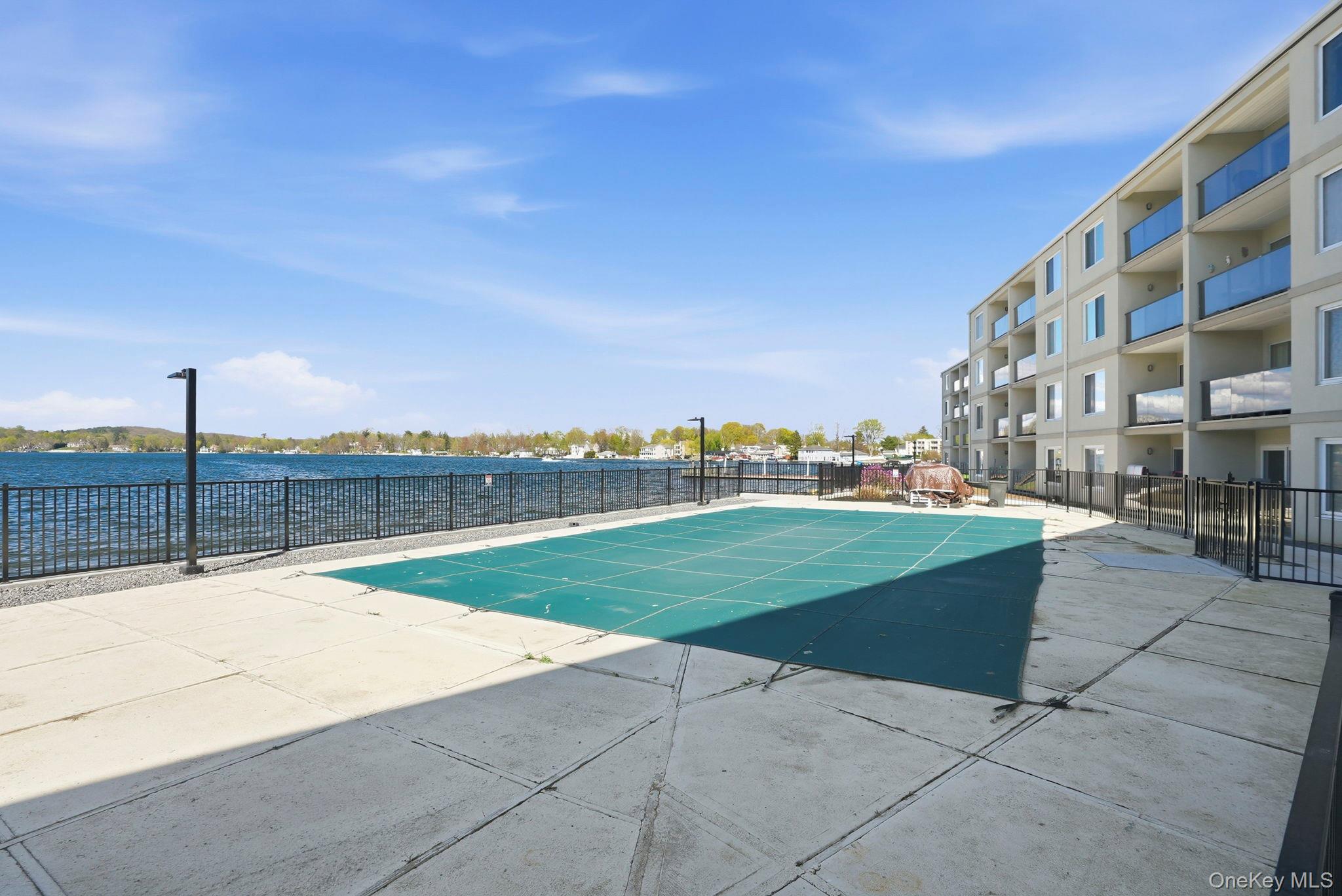 4 Marina Drive, Unit D2 Mahopac, NY 10541 - Photo 26 of 39 Exterior view of the property featuring a covered pool area, surrounded by a concrete patio and black fencing