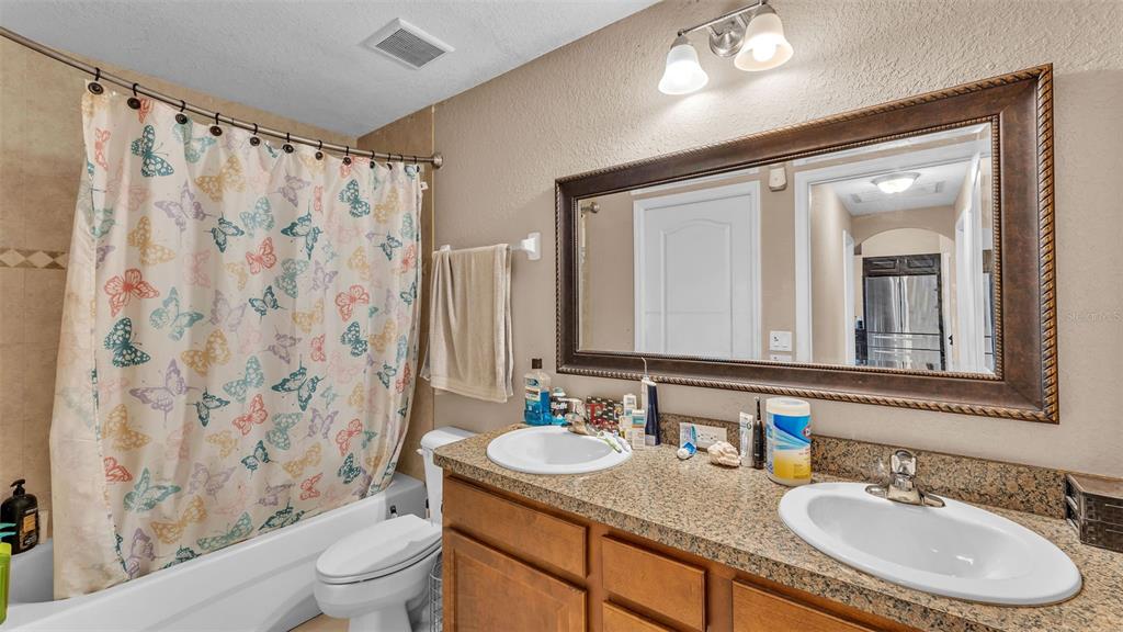 39360 Sparkman Road Dade City, FL 33525 - Photo 20 of 40 a bathroom with a granite countertop sink a toilet a mirror a shower curtain and a bath tub