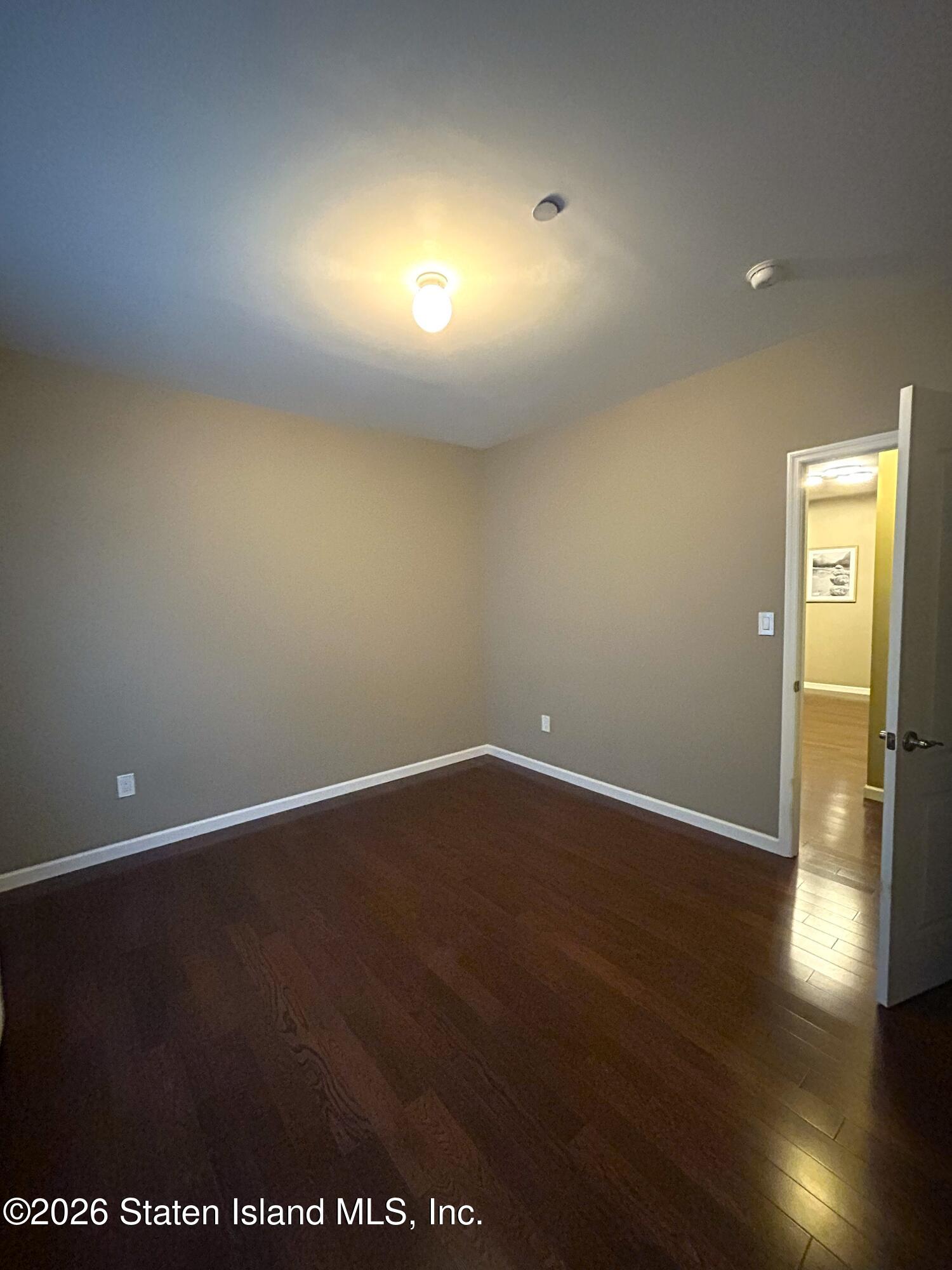 1235 Forest Hill Road, Unit 1G Staten Island, NY 10314 - Photo 8 of 11 an empty room with wooden floor and windows