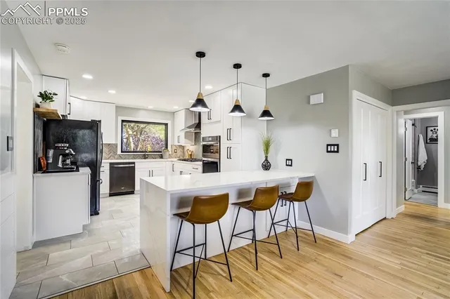 a kitchen with stainless steel appliances kitchen island granite countertop a refrigerator a stove and white cabinets with wooden floor