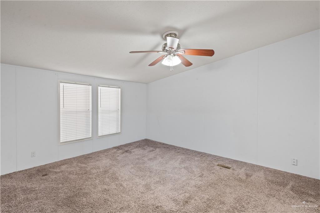 215 South Valley View Road, Unit 252 Donna, TX 78537 - Photo 9 of 19 Spacious room with plush carpet flooring, two windows with blinds, and a ceiling fan with integrated lighting