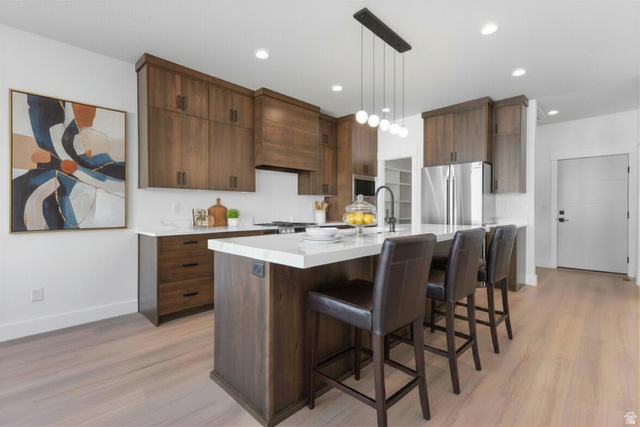 710 East Mountain Road North Ogden, UT 84414 - Photo 8 of 36 Enhanced staged photo Kitchen with a breakfast bar area, stainless steel appliances, an island with sink, light wood finished floors, and hanging light fixtures