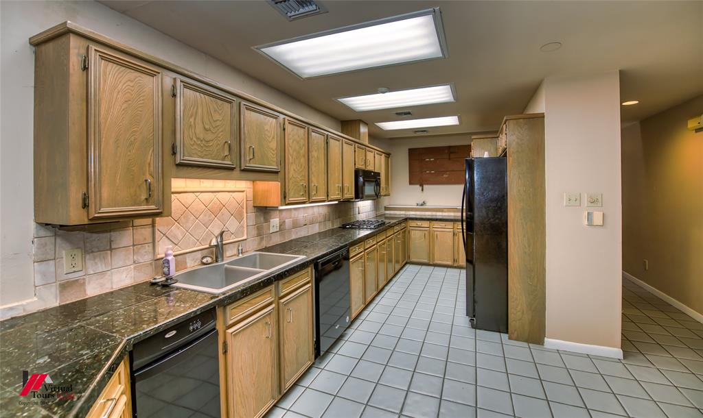 300 Pierremont Road, Unit 40 Shreveport, LA 71106 - Photo 12 of 34 Kitchen featuring extensive wood-finish cabinetry, dark countertops, a double basin stainless steel sink, and a tiled backsplash