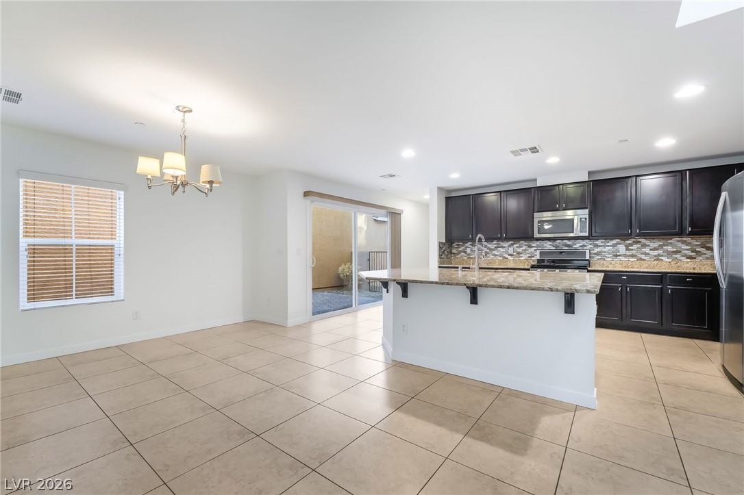 3052 Camino Rico Avenue Henderson, NV 89044 - Photo 12 of 39 Kitchen featuring light stone countertops, backsplash, a kitchen breakfast bar, stainless steel appliances, and dark cabinets