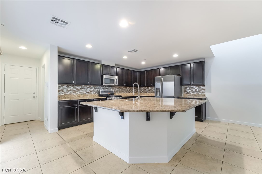 3052 Camino Rico Avenue Henderson, NV 89044 - Photo 13 of 39 Kitchen with light stone counters, light tile patterned floors, stainless steel appliances, decorative backsplash, and a kitchen island with sink