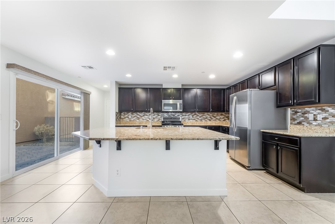 3052 Camino Rico Avenue Henderson, NV 89044 - Photo 14 of 39 Kitchen with light stone counters, stainless steel appliances, a breakfast bar area, a kitchen island with sink, and tasteful backsplash