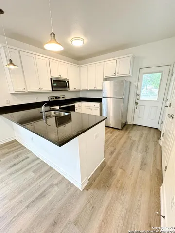 a kitchen with granite countertop a refrigerator a sink dishwasher and white cabinets with wooden floor