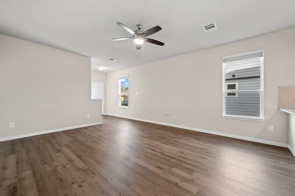 an empty room with wooden floor fan and windows