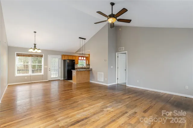 an empty room with wooden floor chandelier fan and windows