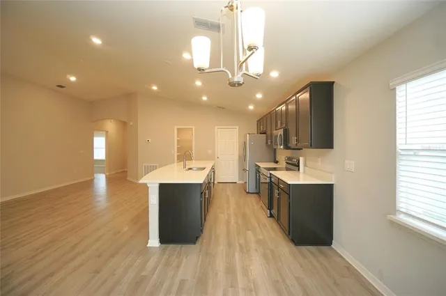 a kitchen with stainless steel appliances kitchen island granite countertop a stove top oven a sink dishwasher a refrigerator and a dining table with wooden floor