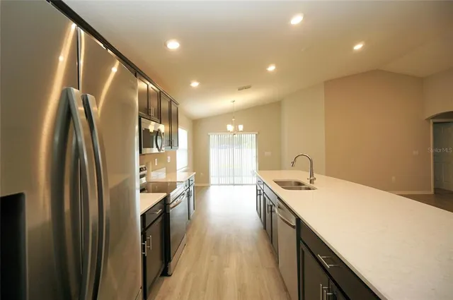 a large kitchen with a large counter top a sink a refrigerator and wooden floor