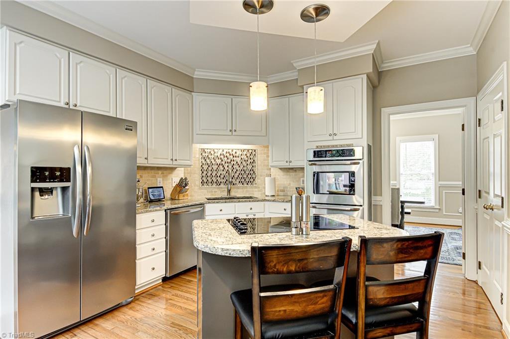 3835 Edgewater Street High Point, NC 27265 - Photo 8 of 30 The kitchen with granite, a tiled back splash, island with smooth surface cook top, pantry, wood flooring, double ovens, and stainless appliances.