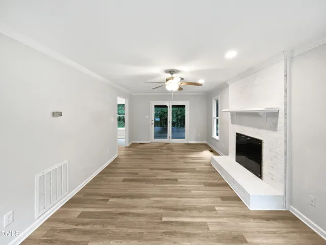 a view of an empty room with wooden floor and a fireplace