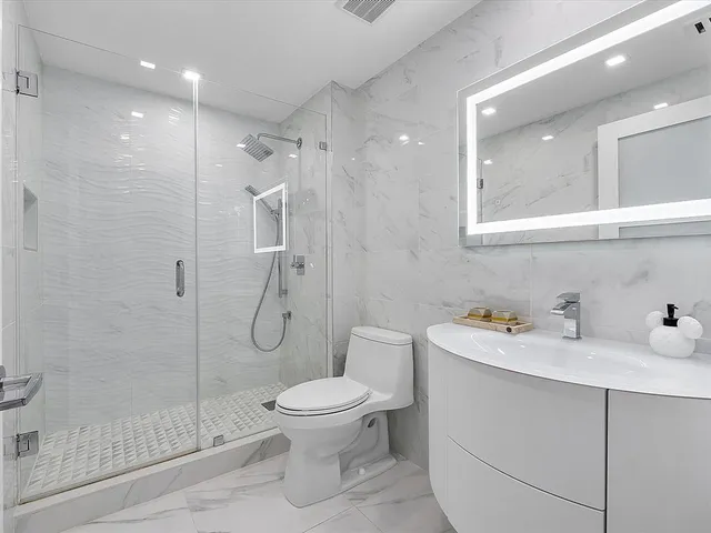 a bathroom with a toilet sink vanity granite and shower