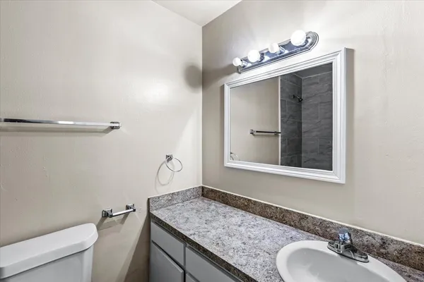 a bathroom with a granite countertop sink a toilet and mirror
