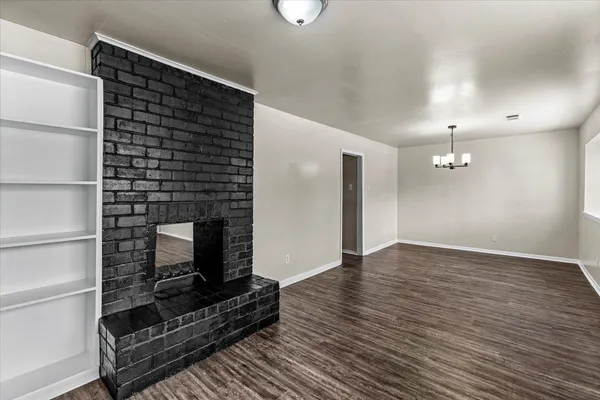 a view of an empty room with wooden floor fire place and a window
