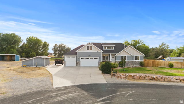 4557 North Ranch Road East Tooele, UT 84074 - Photo 3 of 43 Modern farmhouse exterior featuring light blue siding, stone accents, two attached two-car garages, and a paved driveway