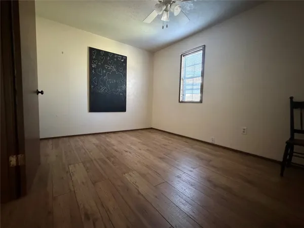 an empty room with wooden floor chandelier fan and windows
