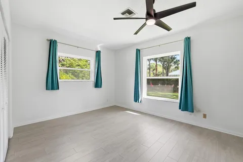 an empty room with wooden floor chandelier fan and windows