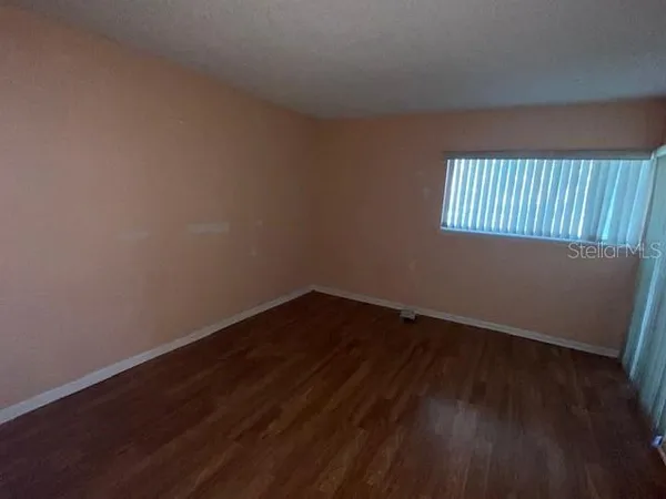 a view of an empty room with wooden floor and a window