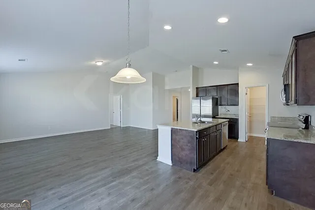 a kitchen with stainless steel appliances granite countertop a stove a refrigerator a sink a oven and a large island with wooden floor