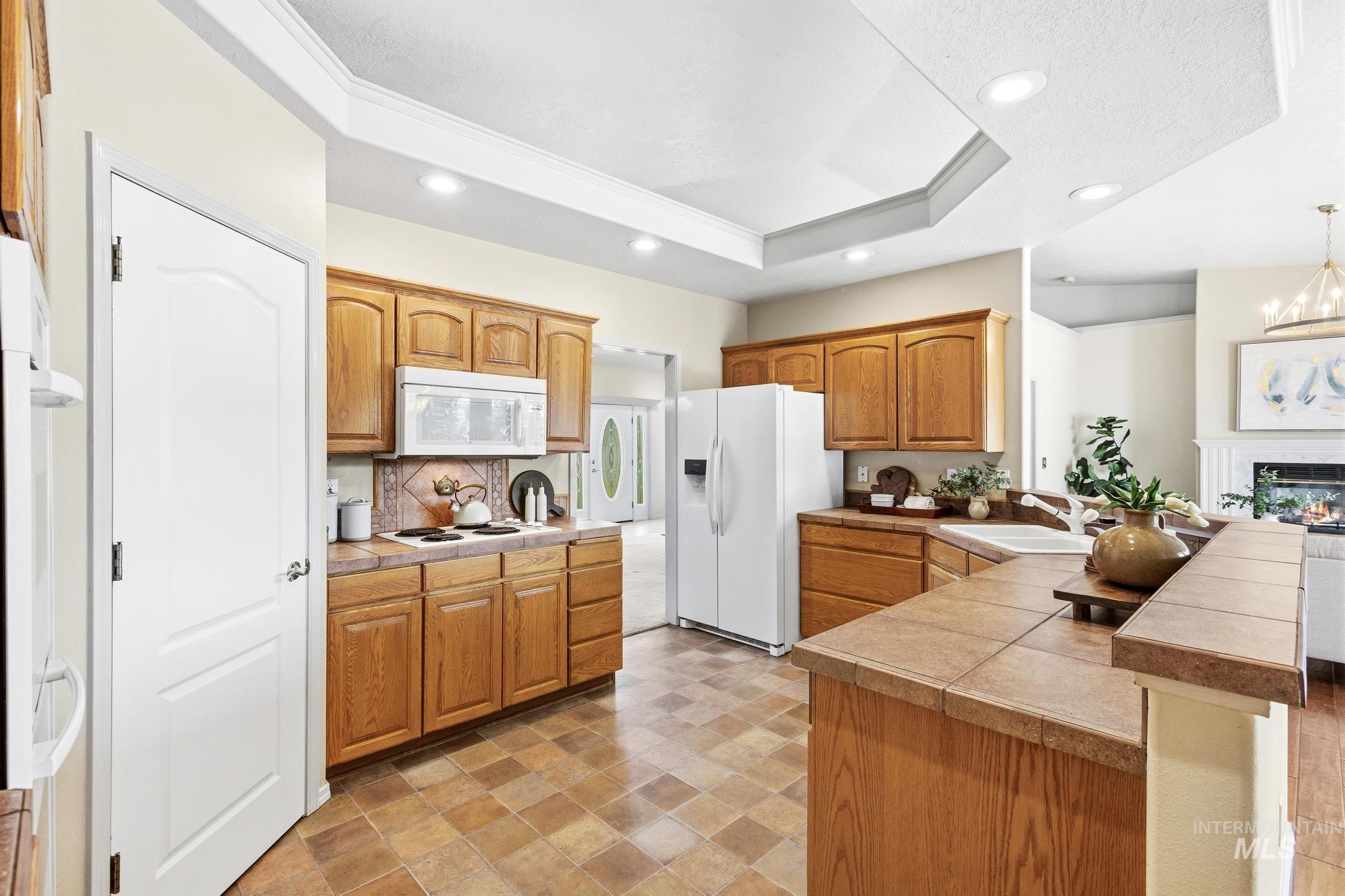 15181 Drury Way Caldwell, ID 83607 - Photo 18 of 49 Kitchen featuring wood cabinetry, tile countertops, tile flooring, white appliances, and a tray ceiling with recessed lighting