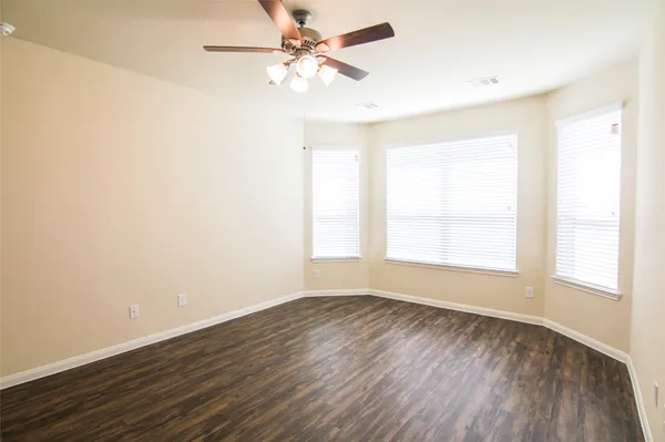 an empty room with wooden floor fan and windows