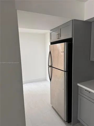 a view of a refrigerator in kitchen and an empty room