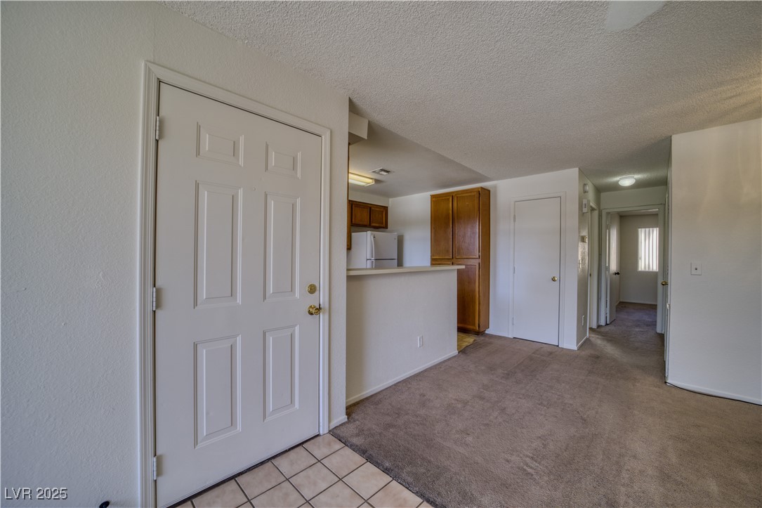 2232 Aspen Mirror Way, Unit 202 Laughlin, NV 89029 - Photo 11 of 39 Kitchen featuring brown cabinets, light carpet, a textured ceiling, freestanding refrigerator, and light tile patterned floors