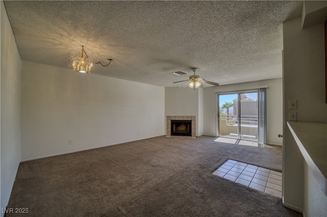 2232 Aspen Mirror Way, Unit 202 Laughlin, NV 89029 - Photo 13 of 39 Unfurnished living room featuring dark carpet, a textured ceiling, a ceiling fan, a tile fireplace, and a chandelier