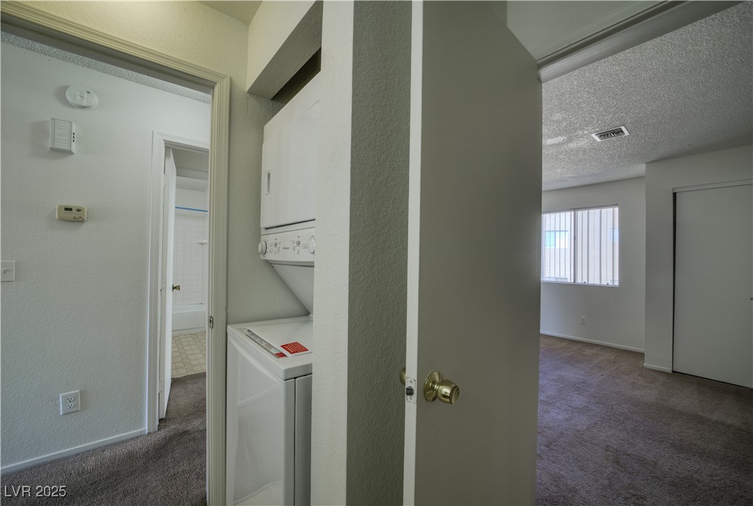 2232 Aspen Mirror Way, Unit 202 Laughlin, NV 89029 - Photo 18 of 39 Laundry area featuring dark colored carpet, a textured ceiling, estacked washer and dryer, and a textured wall