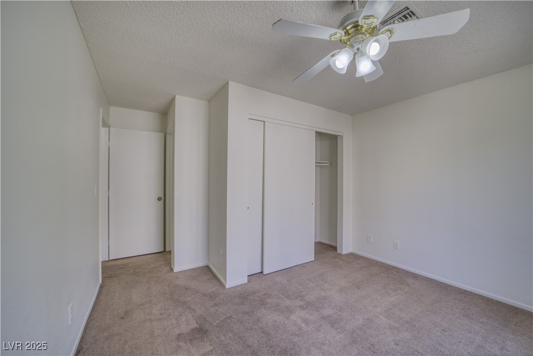 2232 Aspen Mirror Way, Unit 202 Laughlin, NV 89029 - Photo 21 of 39 Unfurnished bedroom featuring light carpet, a textured ceiling, a ceiling fan, and a closet