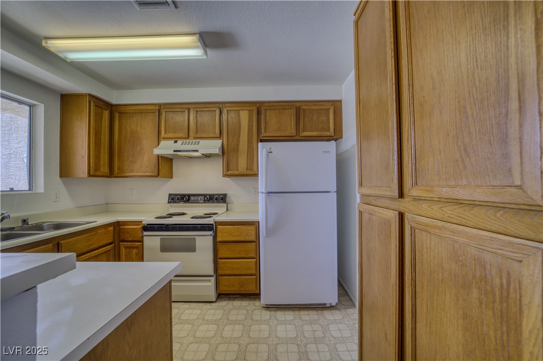 2232 Aspen Mirror Way, Unit 202 Laughlin, NV 89029 - Photo 6 of 39 Kitchen with white appliances, brown cabinetry, light countertops, under cabinet range hood, and light flooring