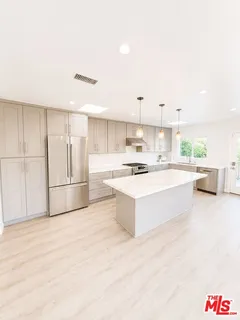 a large white kitchen with kitchen island a stove a sink dishwasher and a refrigerator with wooden floor
