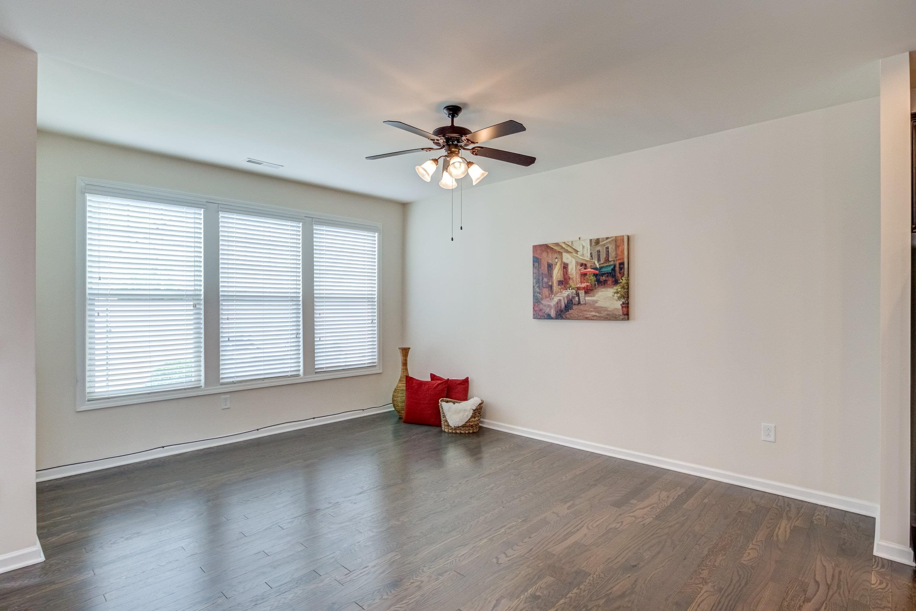 7817 Elmshire Way Raleigh, NC 27616 - Photo 19 of 46 an empty room with wooden floor chandelier fan and windows