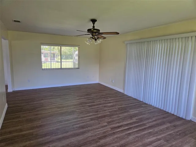 an empty room with wooden floor ceiling fan and windows