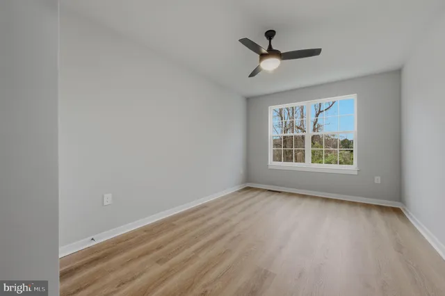 an empty room with wooden floor ceiling fan and windows