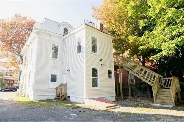 a view of a white house with a small yard and large tree