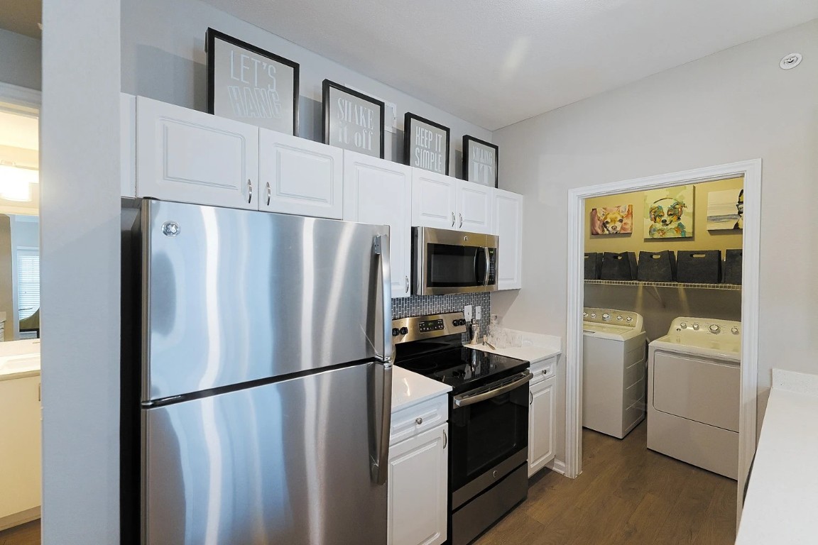 10505 South I-35 Frontage Road, Unit 338 Austin, TX 78747 - Photo 10 of 20 Kitchen featuring stainless steel appliances, washer and clothes dryer, light countertops, white cabinetry, and dark wood-style floors