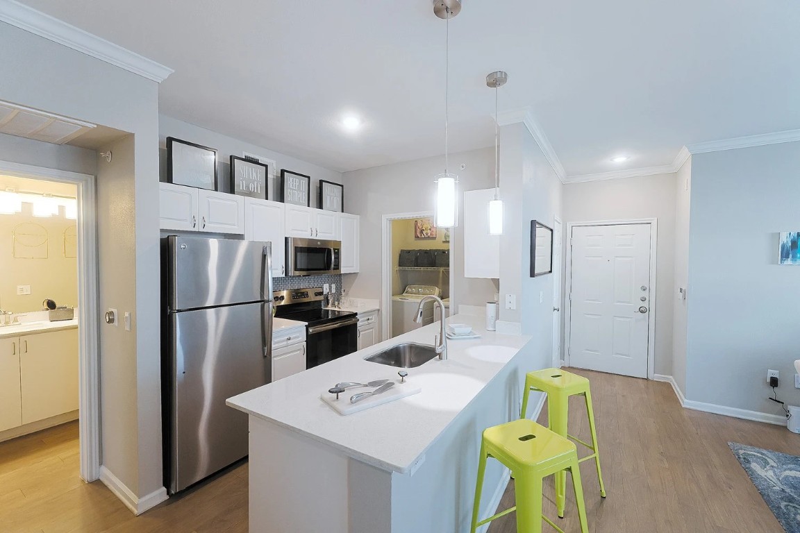 10505 South I-35 Frontage Road, Unit 338 Austin, TX 78747 - Photo 9 of 20 Kitchen with ornamental molding, a peninsula, stainless steel appliances, hanging light fixtures, and a breakfast bar
