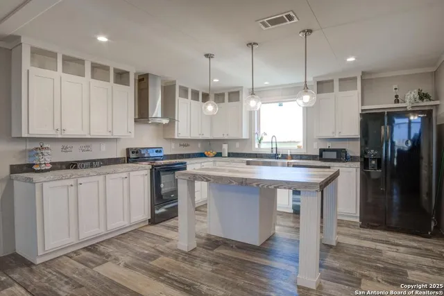 a kitchen with stainless steel appliances granite countertop a sink a stove a refrigerator and island with wooden floor