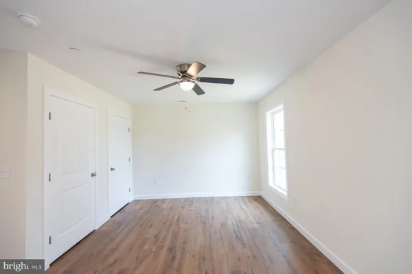 an empty room with wooden floor fan and windows
