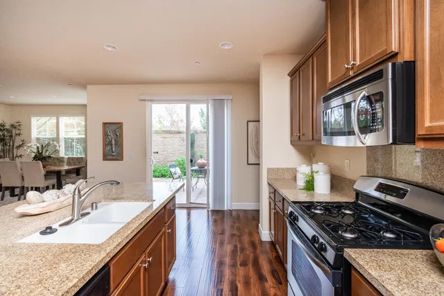 a kitchen with stainless steel appliances granite countertop a stove top oven a sink dishwasher a dining table and chairs with wooden floor