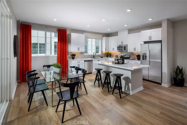 a kitchen with stainless steel appliances kitchen island granite countertop a dining table chairs and a refrigerator